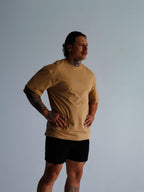 Person wearing a beige t-shirt and black shorts against a plain background