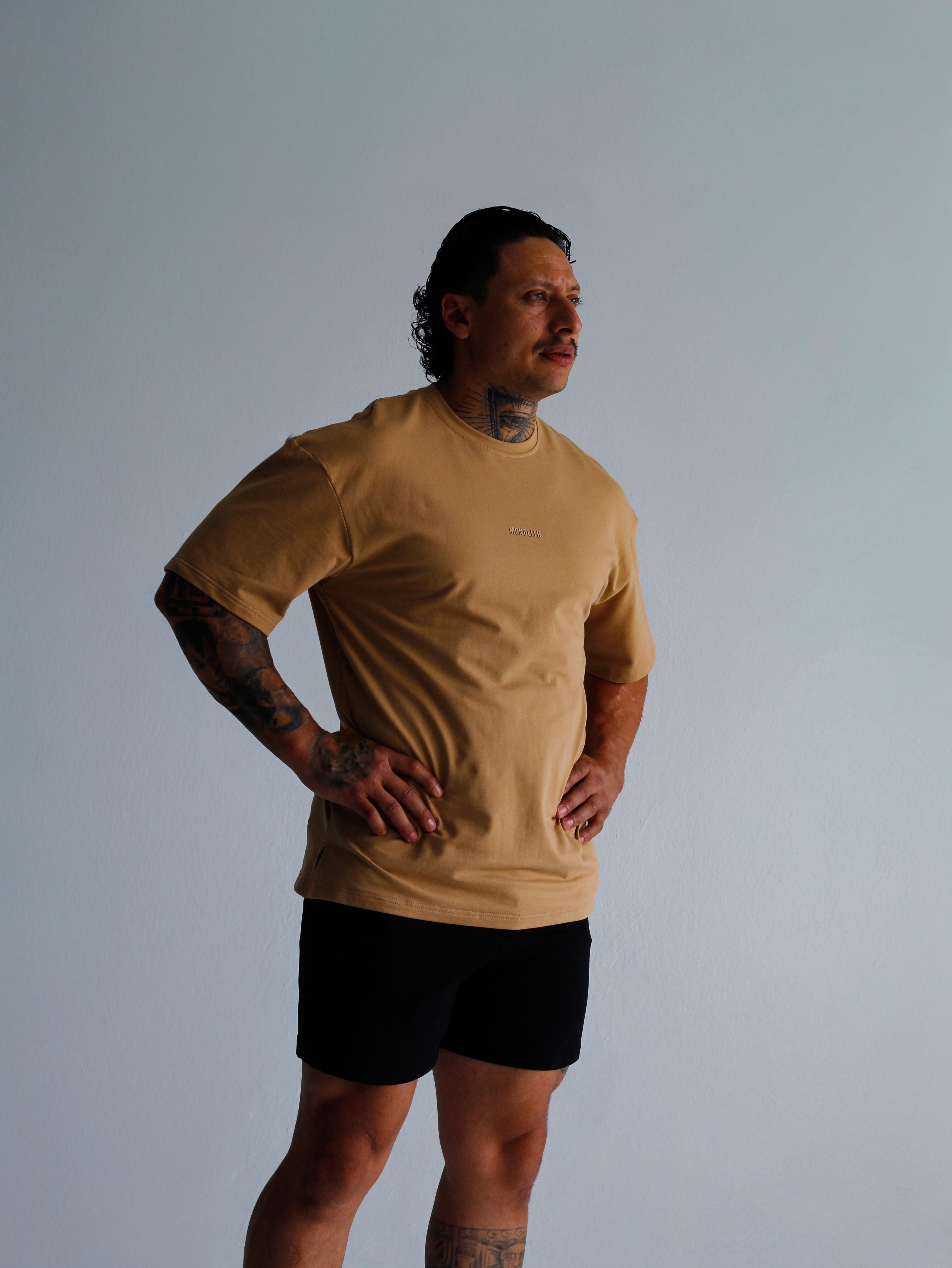 Person wearing a beige t-shirt and black shorts against a plain background