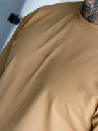 Beige t-shirt with a brand logo on the chest against a neutral background