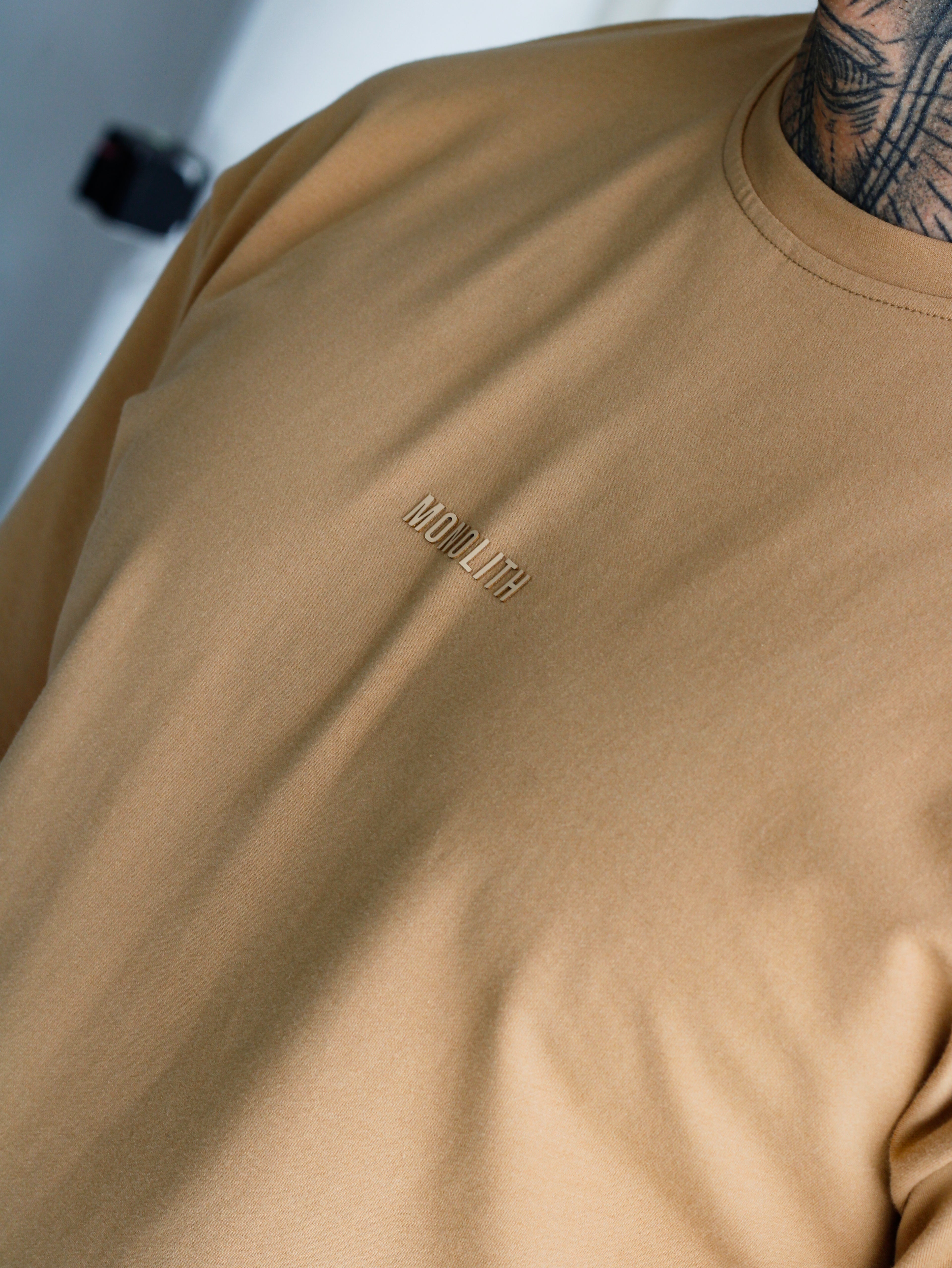 Beige t-shirt with a brand logo on the chest against a neutral background