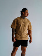 Man wearing a beige t-shirt and black shorts against a light gray background
