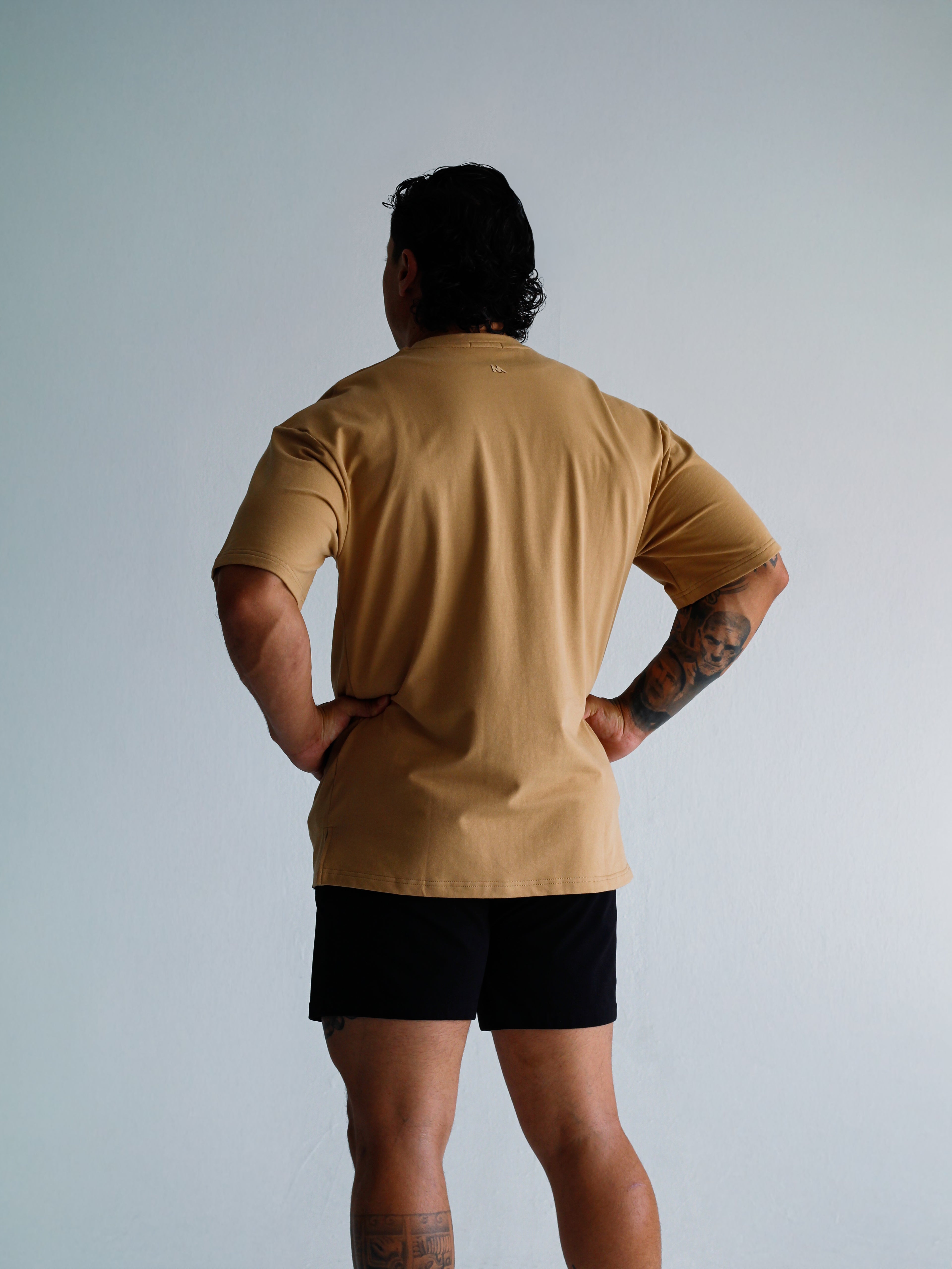 Person wearing a beige t-shirt and black shorts against a light gray background