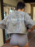 Person wearing a 'Lifting Club' shirt and shorts on a brick patio.