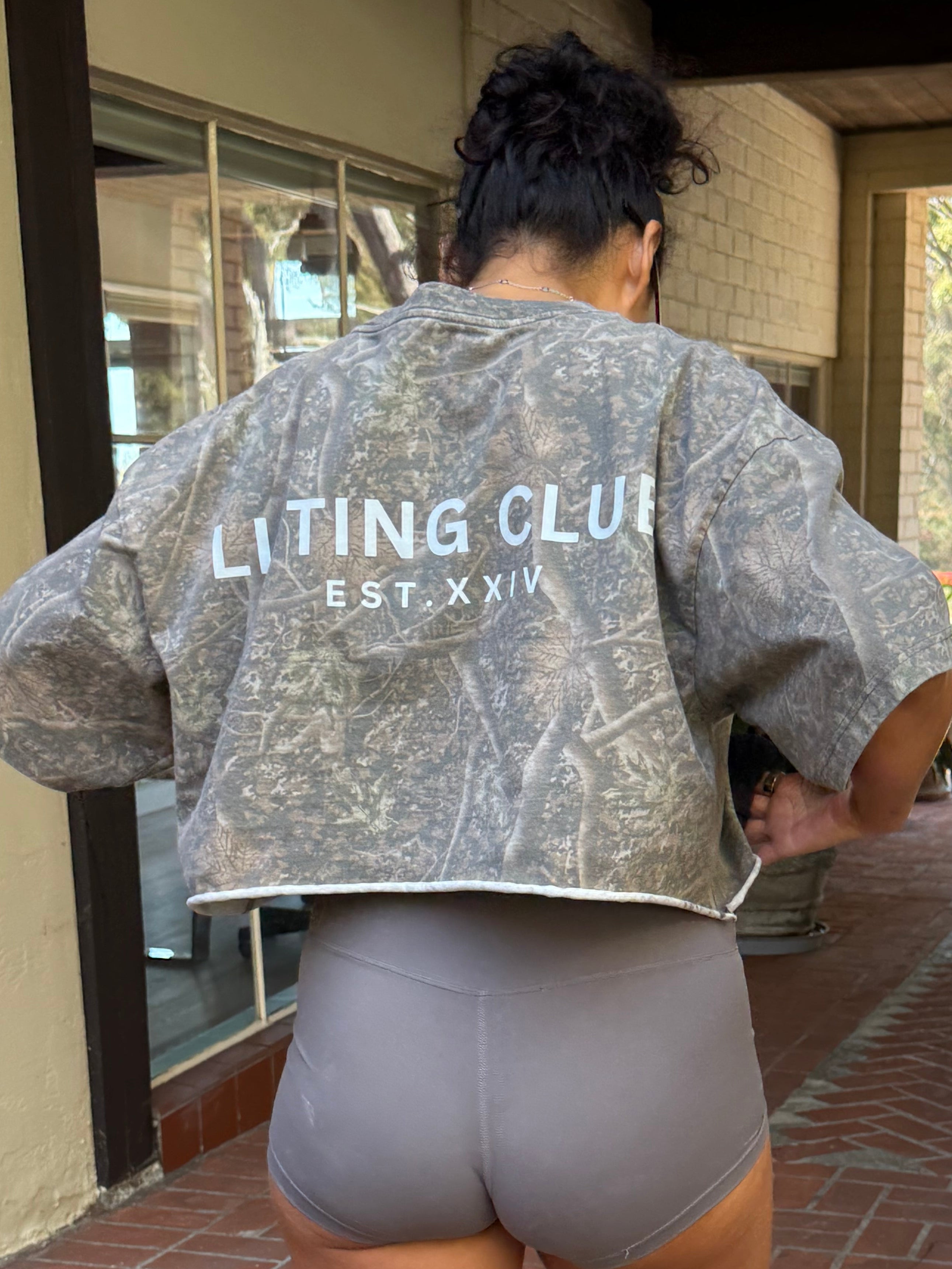 Person wearing a 'Lifting Club' shirt and shorts on a brick patio.